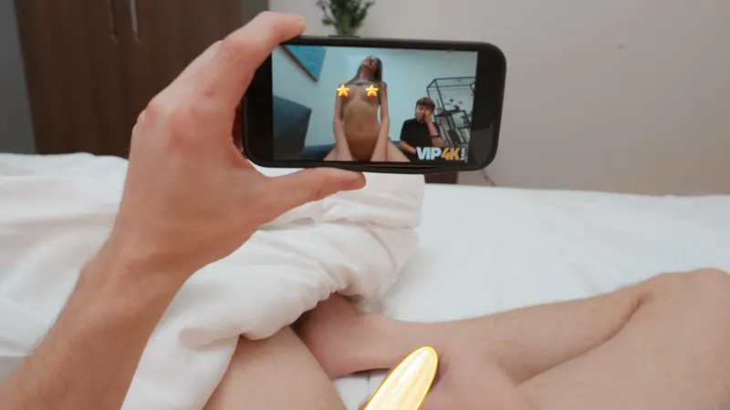 The guest lies alone in bed, holding up a phone playing porn (censored)