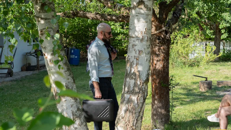 The husband stops between the birch trees, briefcase in hand, scanning the garden