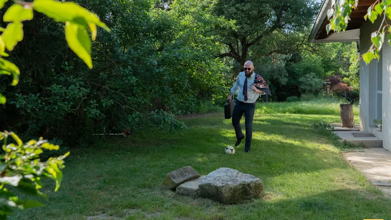 A bearded man in a shirt and tie walks across the lawn carrying a briefcase
