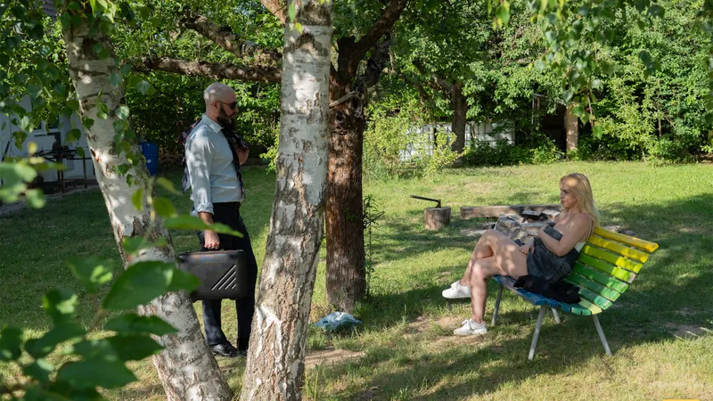 The husband stands between the birch trees while Millie sits on a colorful bench nearby